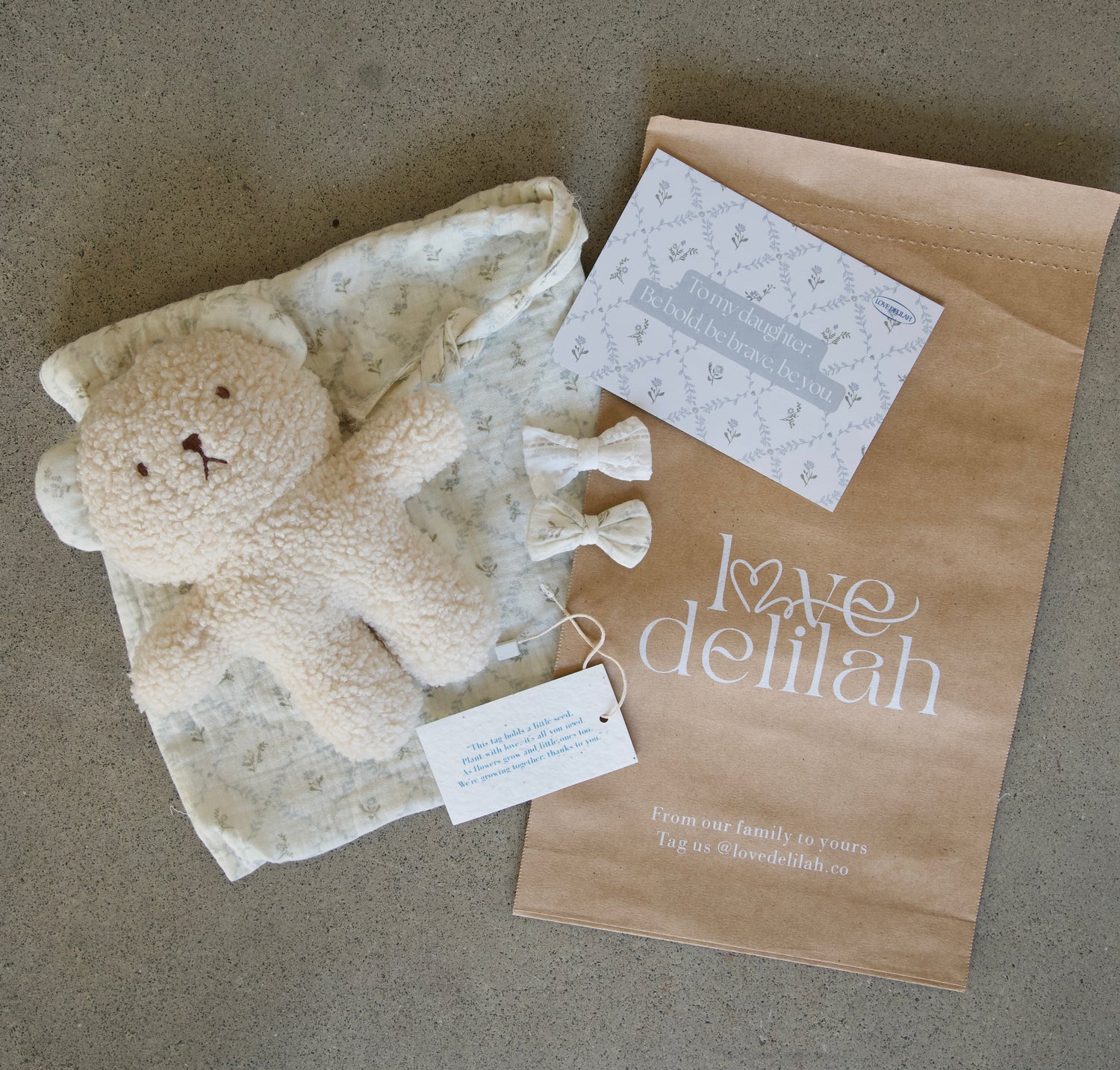 Baby gift set with teddy bear, blanket, and card on a brown surface